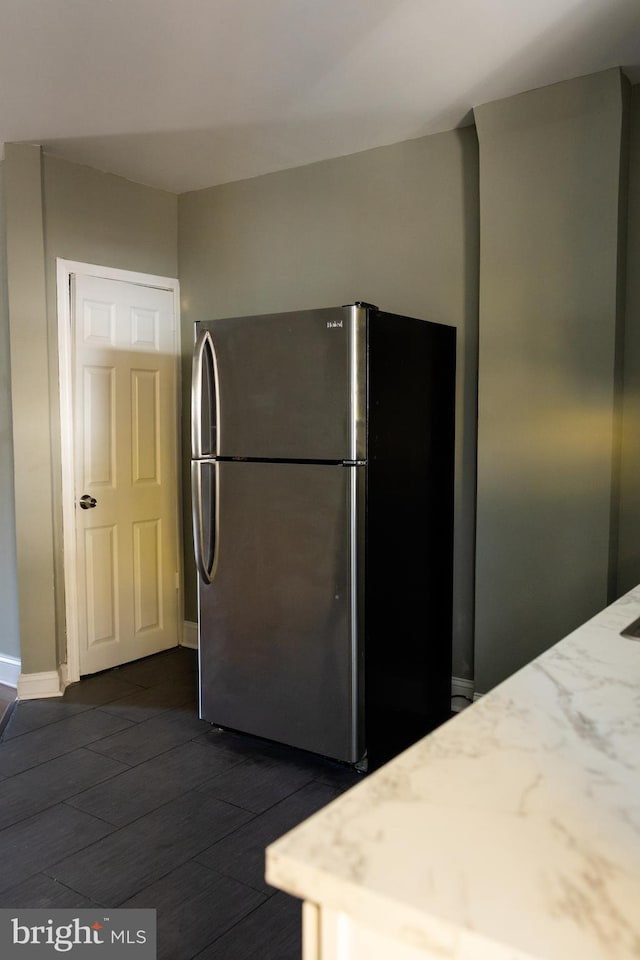 kitchen with stainless steel fridge, dark wood-type flooring, and light stone counters