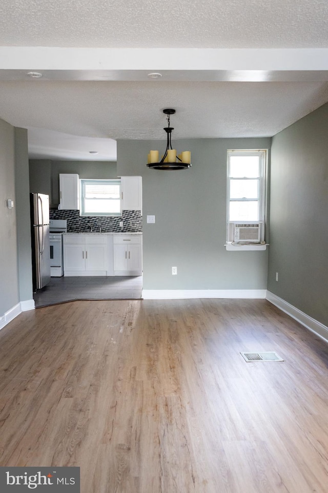 unfurnished living room with cooling unit, a textured ceiling, and light wood-type flooring