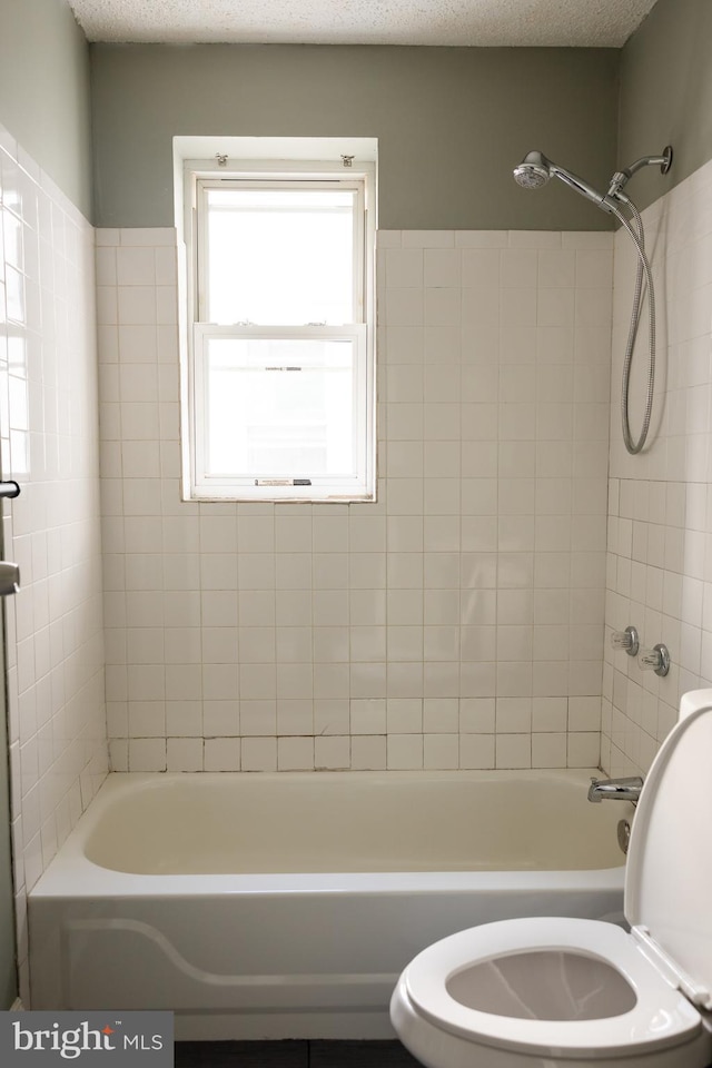 bathroom featuring toilet, a textured ceiling, and tiled shower / bath