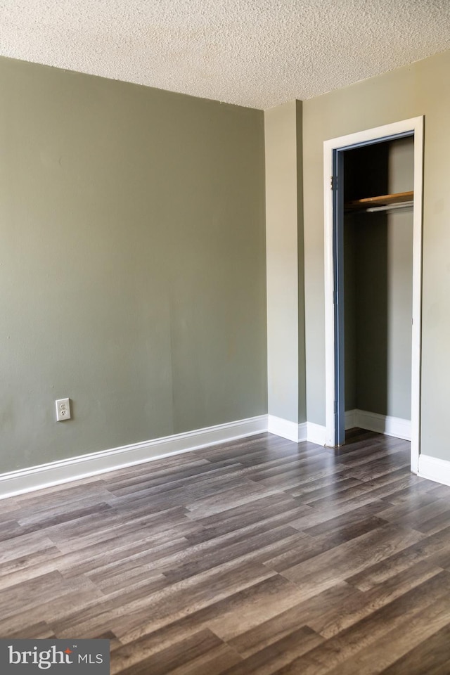 unfurnished bedroom featuring a textured ceiling, dark wood-type flooring, and a closet