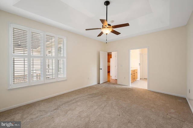 unfurnished bedroom featuring connected bathroom, light colored carpet, ceiling fan, and a tray ceiling