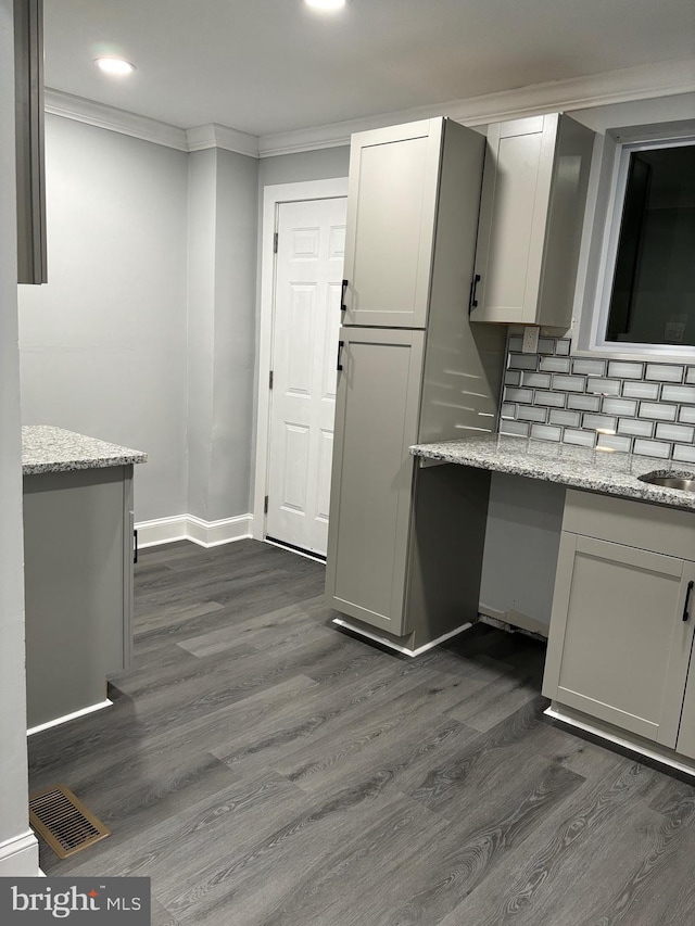 kitchen featuring dark wood-type flooring, sink, light stone counters, crown molding, and tasteful backsplash