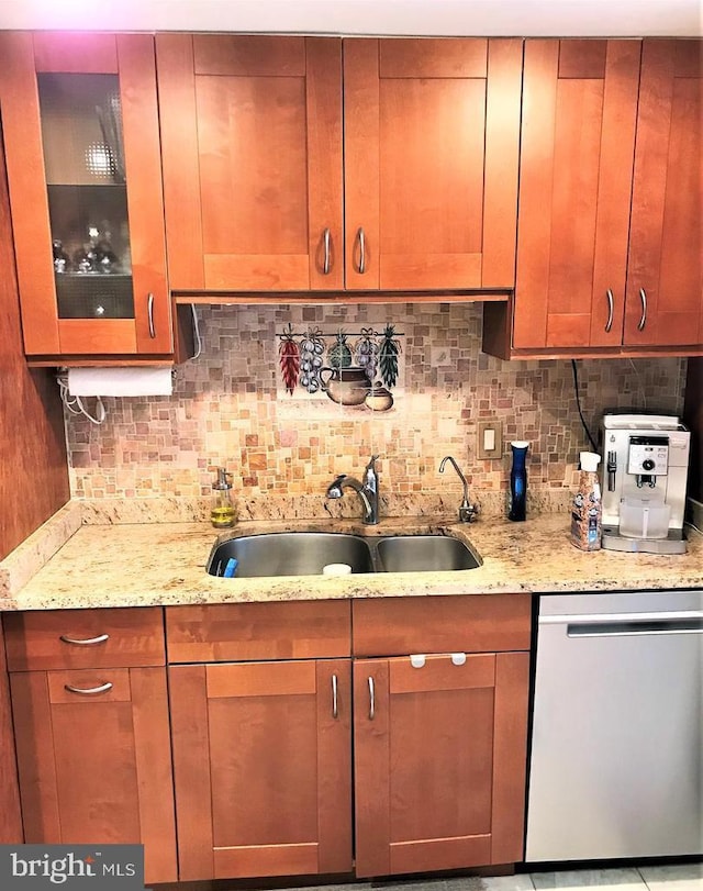 kitchen featuring stainless steel dishwasher, light stone countertops, backsplash, and a sink