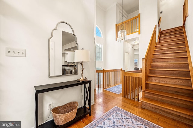 staircase featuring a notable chandelier, wood-type flooring, ornamental molding, and a high ceiling