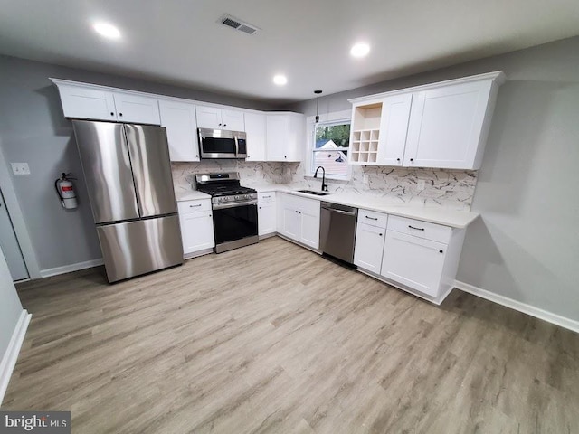 kitchen with appliances with stainless steel finishes, sink, decorative light fixtures, light hardwood / wood-style flooring, and white cabinets