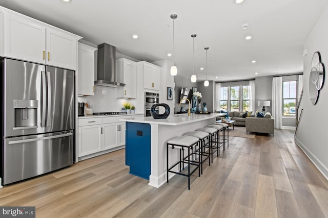 kitchen with appliances with stainless steel finishes, a breakfast bar, wall chimney range hood, pendant lighting, and an island with sink