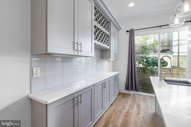 kitchen with gray cabinetry, pendant lighting, backsplash, sink, and light hardwood / wood-style flooring