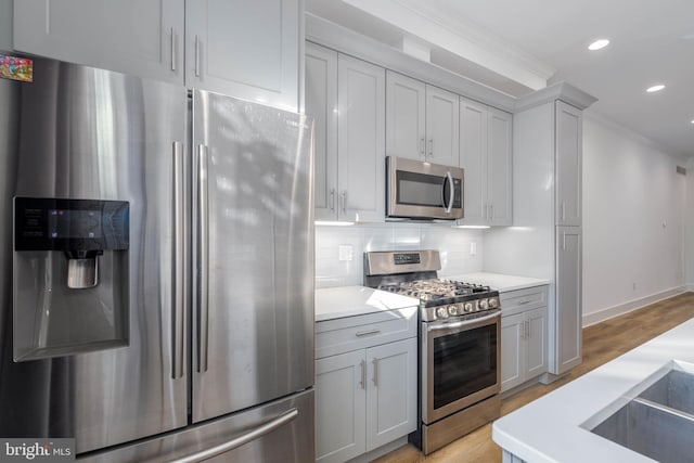 kitchen featuring appliances with stainless steel finishes, backsplash, ornamental molding, light hardwood / wood-style flooring, and gray cabinets