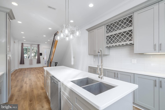 kitchen featuring a kitchen island with sink, sink, stainless steel dishwasher, hardwood / wood-style flooring, and gray cabinets