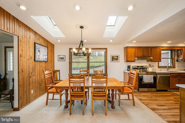 dining room with sink, light hardwood / wood-style flooring, an inviting chandelier, and wood walls