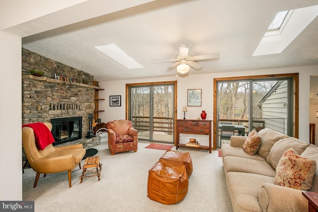 living room featuring carpet floors, a stone fireplace, ceiling fan, and a healthy amount of sunlight