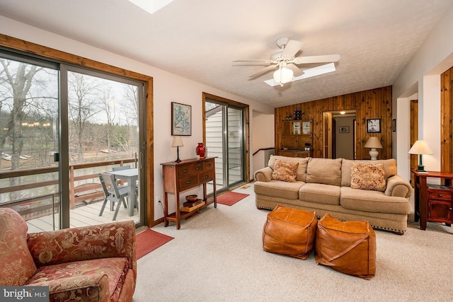 living room featuring lofted ceiling, light colored carpet, ceiling fan, and wooden walls