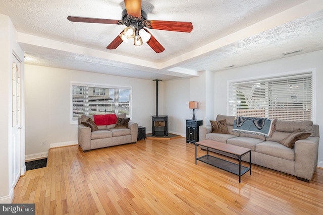 living room with a wood stove, ceiling fan, wood-type flooring, and a textured ceiling