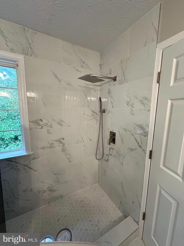 bathroom with tiled shower, a textured ceiling, and plenty of natural light