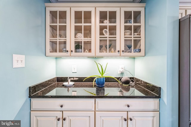 bar with white cabinetry and dark stone countertops