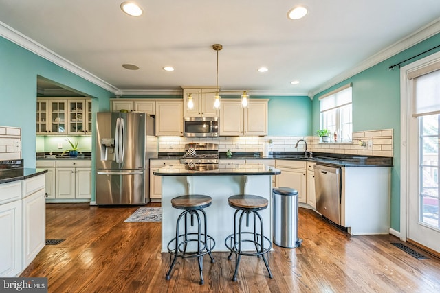 kitchen featuring hardwood / wood-style floors, crown molding, sink, appliances with stainless steel finishes, and decorative light fixtures