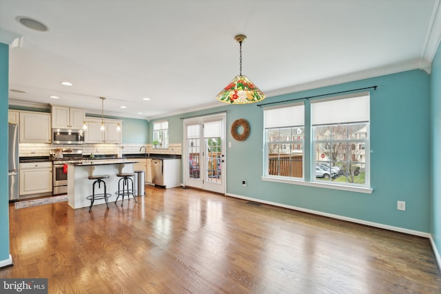 kitchen featuring stainless steel appliances, crown molding, hardwood / wood-style floors, decorative light fixtures, and a breakfast bar