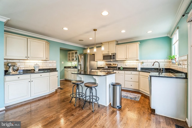 kitchen with stainless steel appliances, crown molding, decorative light fixtures, hardwood / wood-style flooring, and a center island