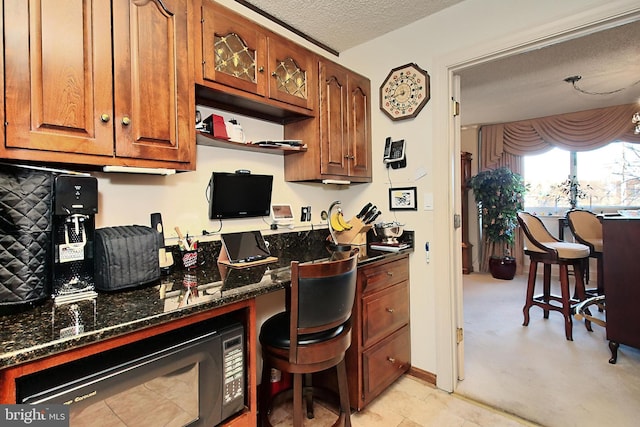 kitchen featuring light colored carpet, a textured ceiling, built in desk, and dark stone countertops