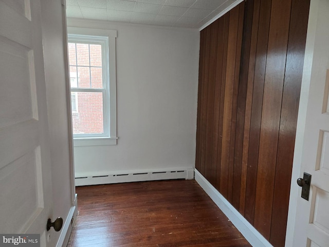 spare room featuring wooden walls, baseboard heating, and dark wood-type flooring