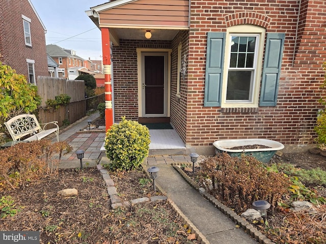 doorway to property featuring fence and brick siding