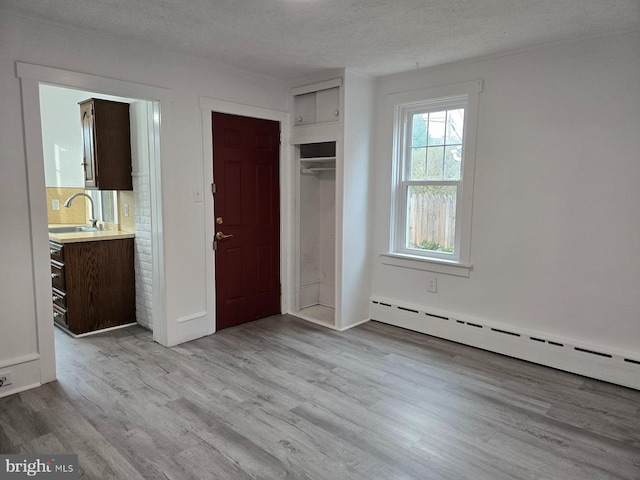 unfurnished bedroom with a textured ceiling, light hardwood / wood-style floors, a baseboard heating unit, and sink