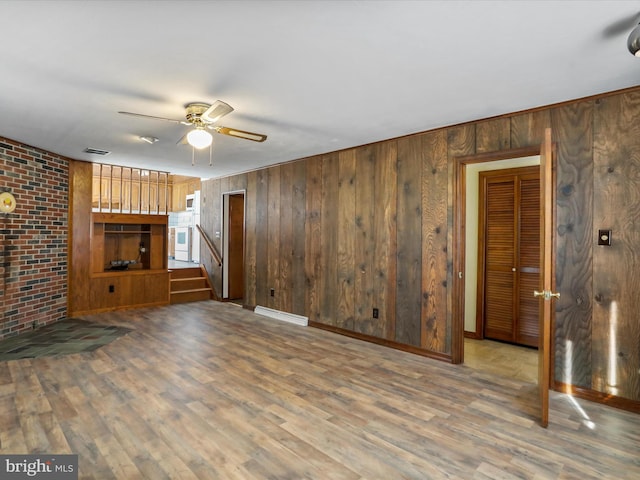 unfurnished living room with brick wall, hardwood / wood-style floors, ceiling fan, and wood walls