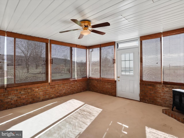 unfurnished sunroom featuring a wood stove, ceiling fan, and wood ceiling