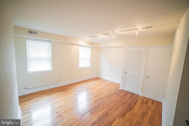 empty room with track lighting and light hardwood / wood-style flooring