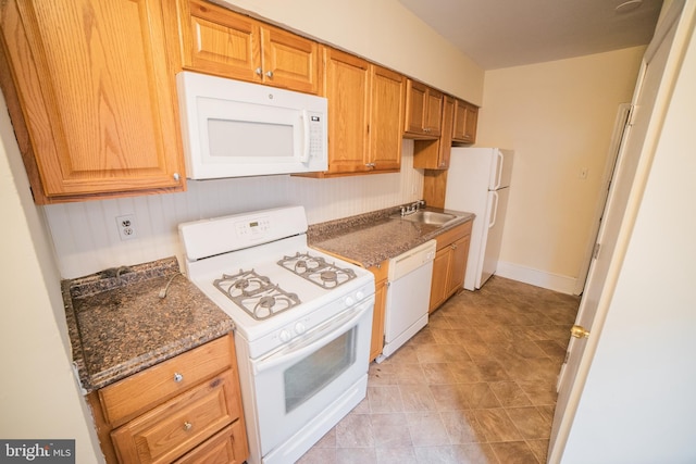 kitchen with white appliances, dark stone counters, and sink