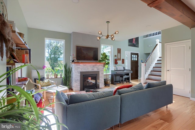 living area with stairway, a stone fireplace, a chandelier, light wood-type flooring, and beamed ceiling