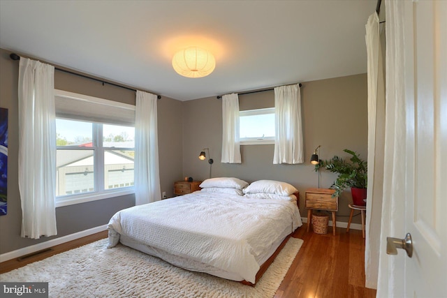 bedroom with baseboards, visible vents, and wood finished floors