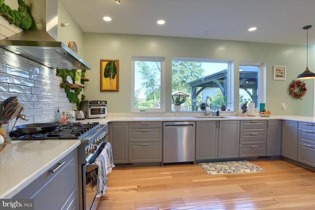 kitchen with light wood-style flooring, gray cabinetry, appliances with stainless steel finishes, a sink, and extractor fan