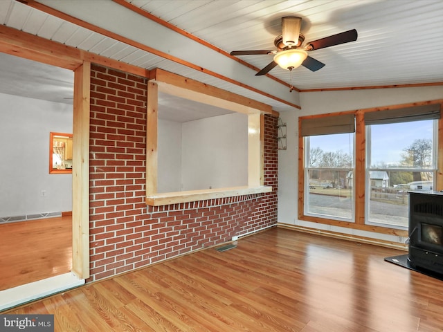 unfurnished living room featuring ceiling fan, brick wall, visible vents, light wood-type flooring, and a wood stove