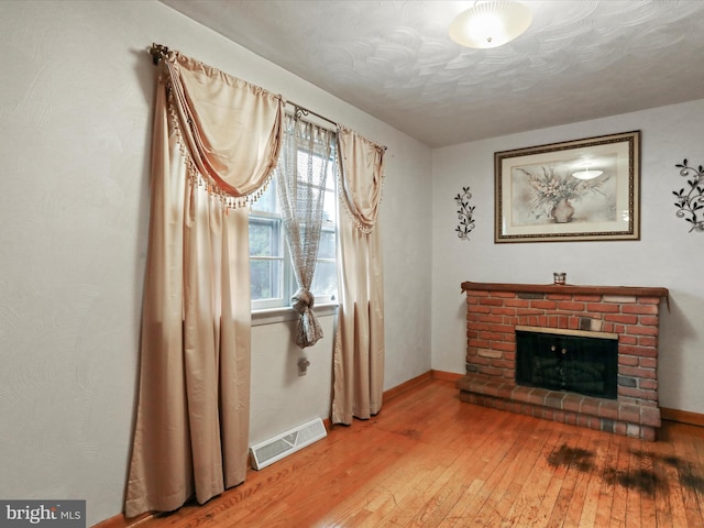 sitting room with a brick fireplace, visible vents, wood-type flooring, and baseboards