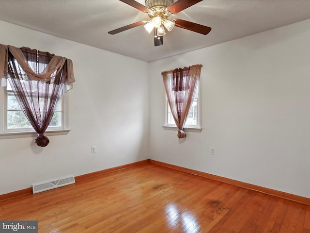 spare room with wood-type flooring, visible vents, ceiling fan, and baseboards