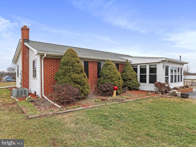 view of front of property with brick siding, roof with shingles, a chimney, central AC, and a front lawn