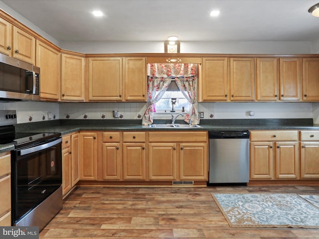 kitchen with dark countertops, wood finished floors, stainless steel appliances, a sink, and recessed lighting