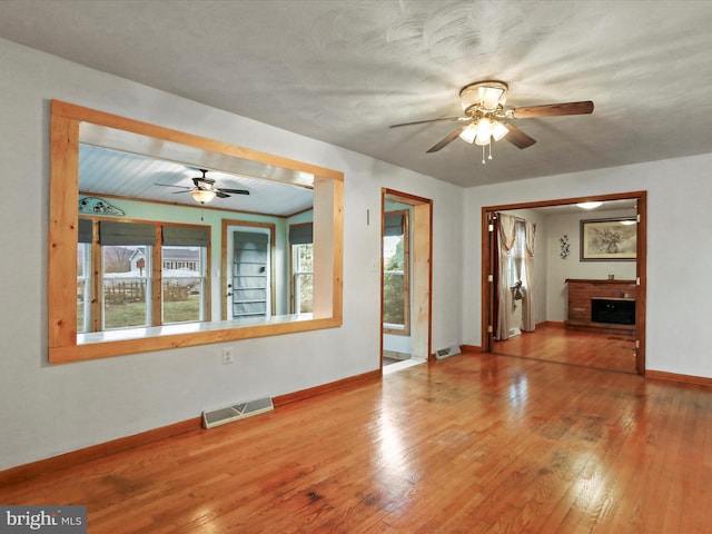 spare room with a fireplace, wood-type flooring, visible vents, ceiling fan, and baseboards