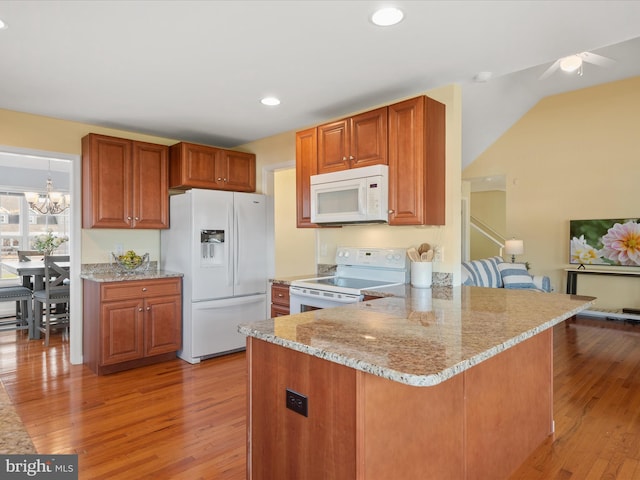 kitchen featuring white appliances, light stone counters, kitchen peninsula, a chandelier, and light wood-type flooring