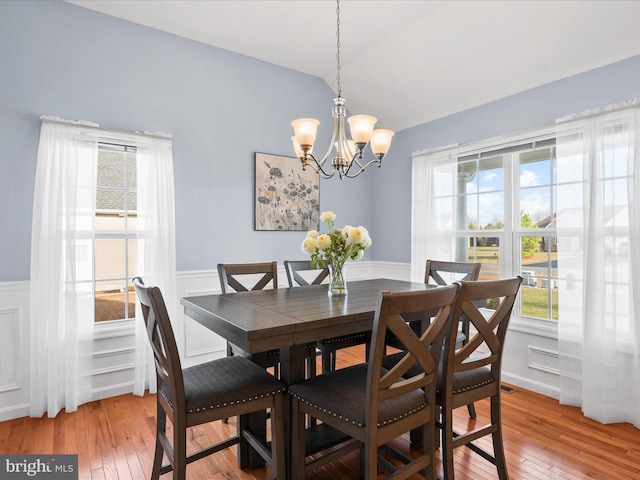 dining space with a notable chandelier, wood-type flooring, and vaulted ceiling