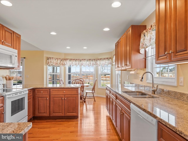 kitchen with white appliances, kitchen peninsula, sink, and light stone countertops