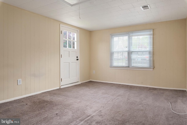 carpeted empty room with a wealth of natural light and wooden walls