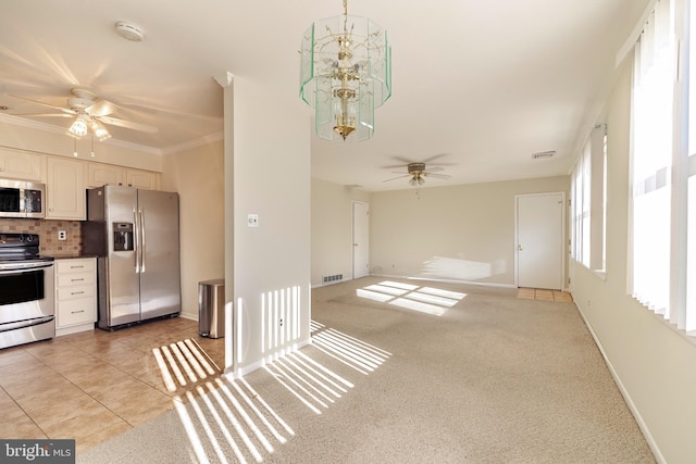 kitchen with tasteful backsplash, crown molding, light tile patterned flooring, ceiling fan with notable chandelier, and appliances with stainless steel finishes