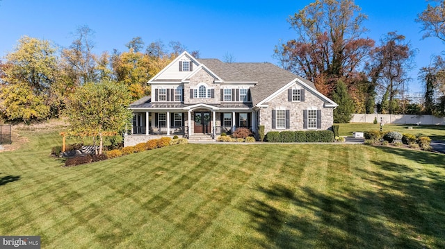 view of front of property featuring stone siding, fence, a front lawn, and covered porch