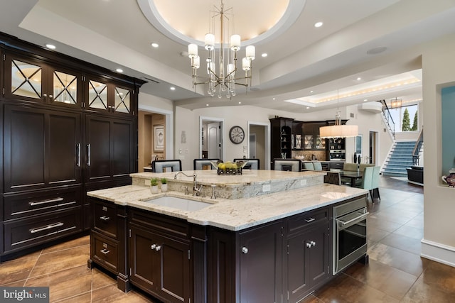 kitchen featuring a tray ceiling, sink, a large island with sink, decorative light fixtures, and oven