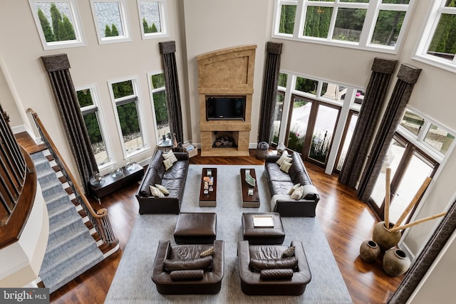 living room with a fireplace, a healthy amount of sunlight, a towering ceiling, and dark wood-type flooring