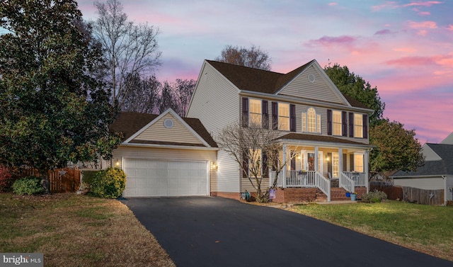 colonial inspired home with a lawn, a garage, and covered porch