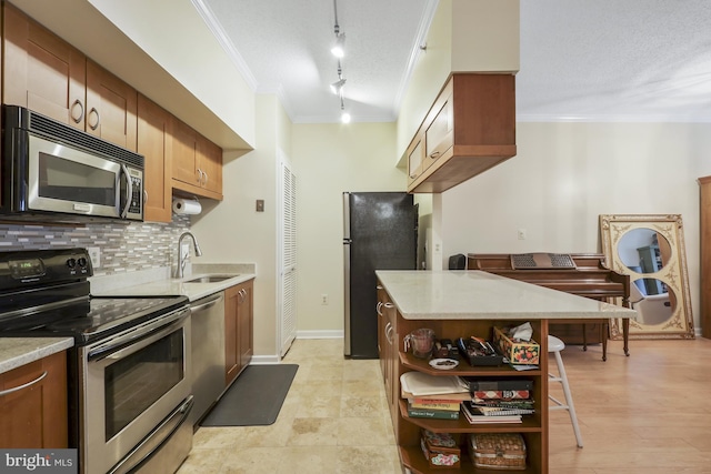 kitchen with appliances with stainless steel finishes, rail lighting, ornamental molding, a textured ceiling, and sink