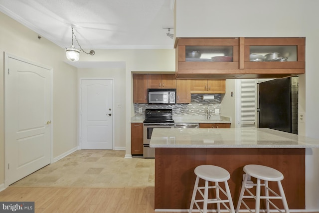 kitchen featuring light stone counters, pendant lighting, a breakfast bar area, appliances with stainless steel finishes, and ornamental molding